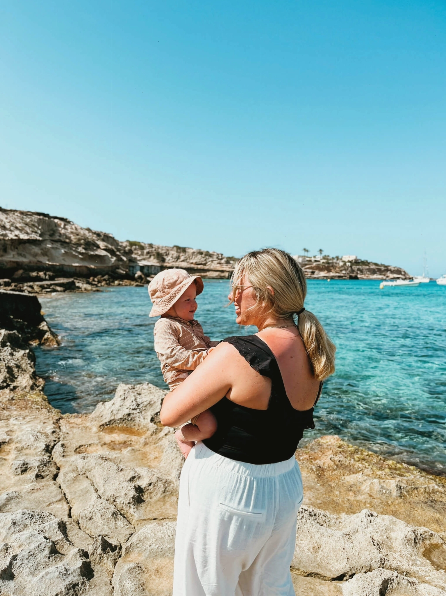 Phụ nữ và trẻ em nhìn nhau trên mỏm đá bên cạnh biển xanh ở Ibiza, Tây Ban Nha